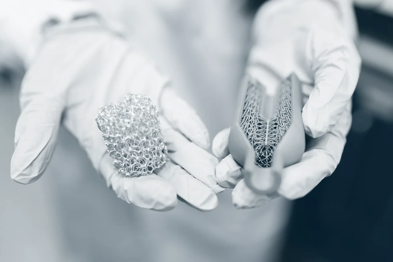 Hände in Laborhandschuhen halten Gitterstrukturen aus dem 3D-Druck, wie sie für Implantate verwendet werden